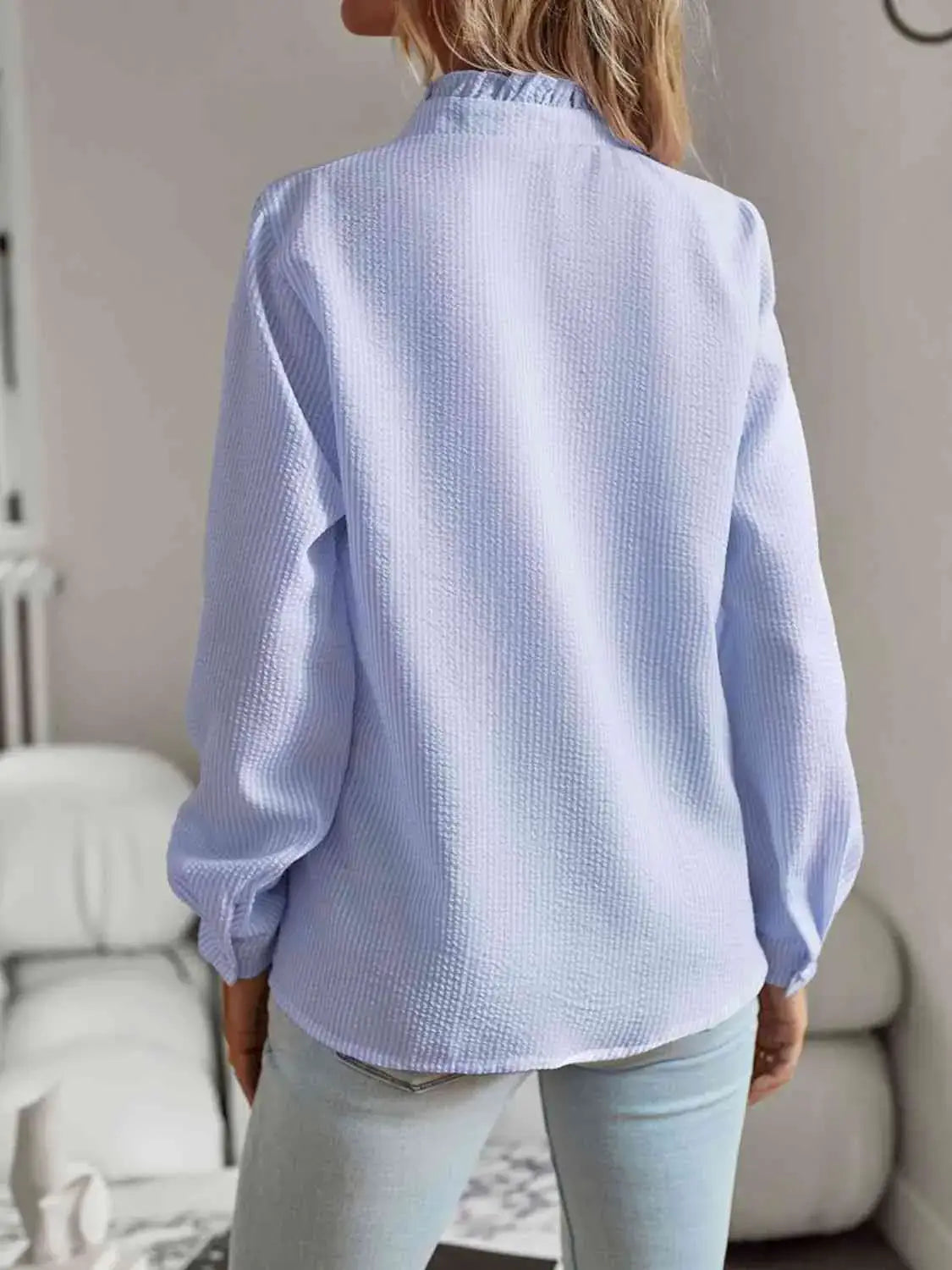 Back view of a light blue ruffle trim long sleeve shirt, showcasing its feminine design and comfortable fit.