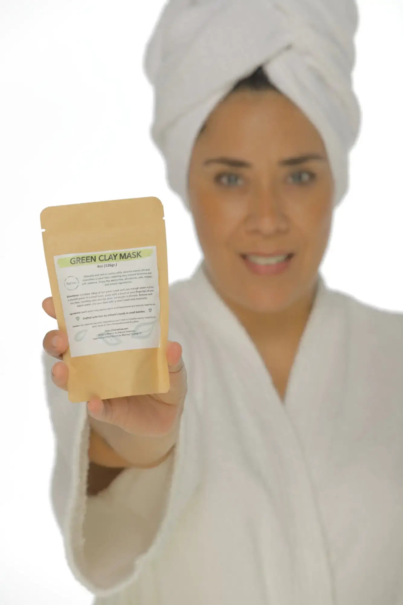 Woman in a white robe holding a Green Clay Mask package, promoting natural detox and deep pore cleansing for healthy skin.