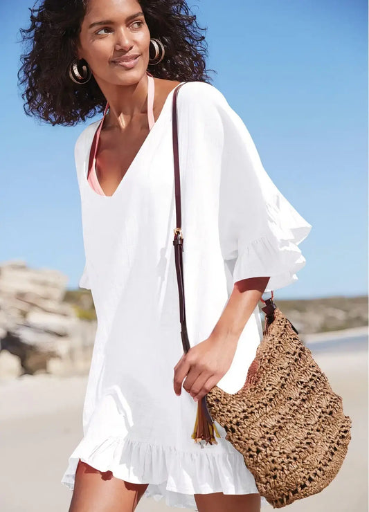 Woman in oversized white ruffle cover-up tunic, perfect for summer beach days, accessorized with a stylish straw bag.