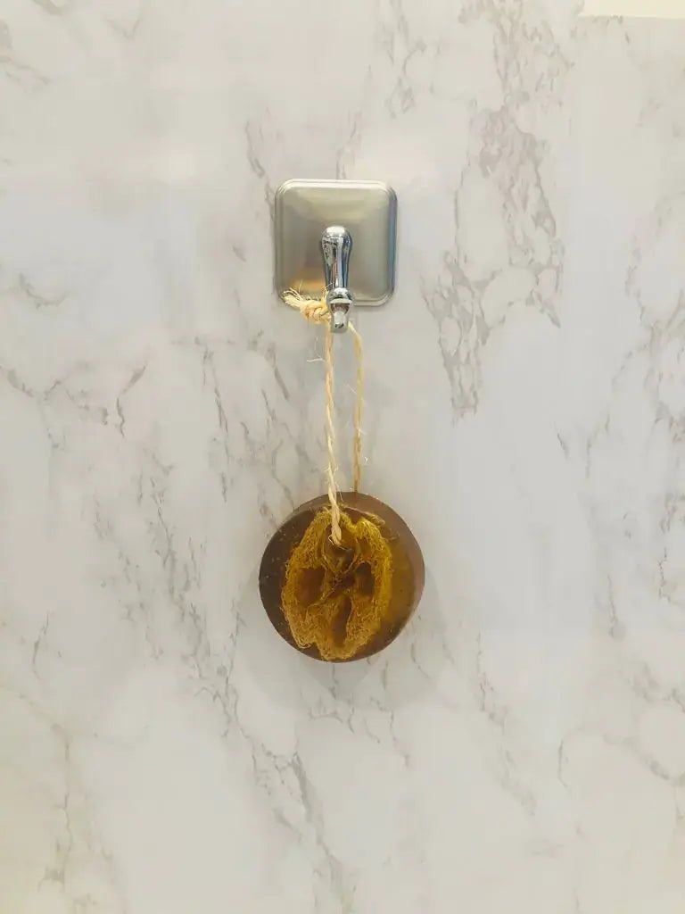 Pristine Soap Bar with loofah hanging on a hook against a marble background.